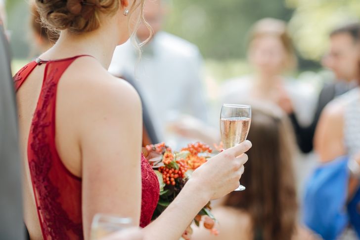 Woman holding a glass of champagne at a summer party. Party outside with chic clothes. Bride with red wedding dress at an outdoor wedding 