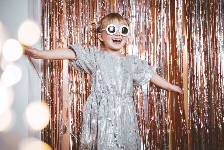 Happy little stylish girl in shiny dress having fun. Festive background with foil curtain decorations for kids birthday or fancy dress party, disco music or New Year. Celebration and Holiday concept.