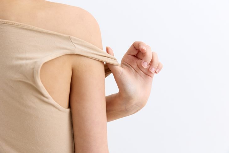 Woman adjusting beige off-shoulder top with delicate hand gesture on light background, showcasing soft skin tone and minimalistic style in natural lighting.